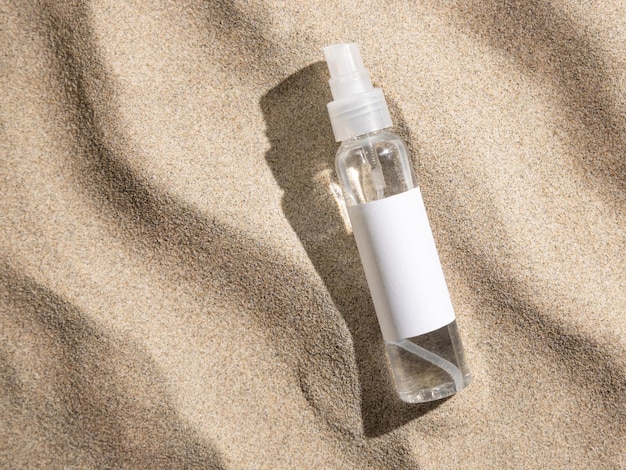 Spray bottle with blank label on beige sand top view hard light\
cosmetic packaging mockup