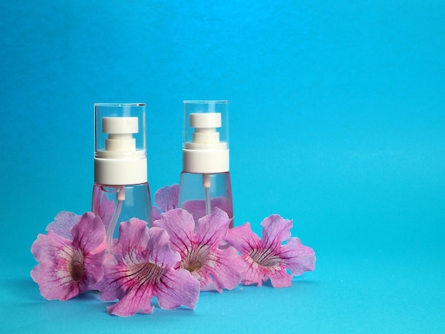 Spray bottles for tonic lotion home cosmetics and large pink\
flowers isolated on a blue background