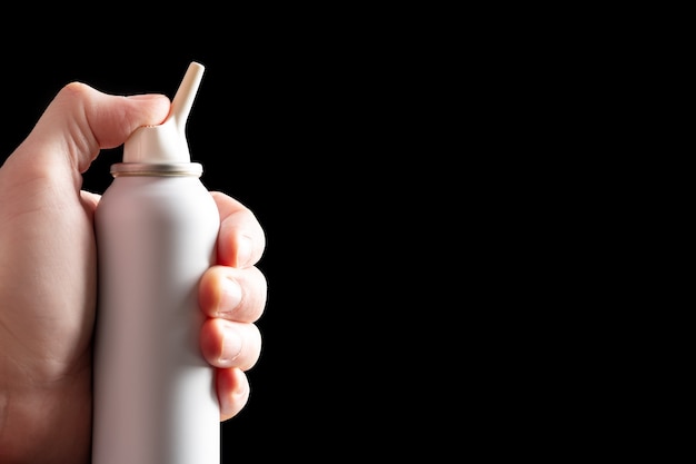 Spray fles met zout zeewater voor neusholte hygiëne in vrouwelijke hand geïsoleerd op zwart hand