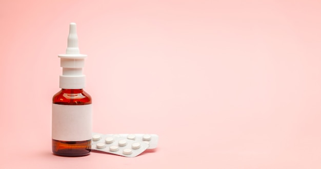 Spray for nose and pills in a blister pack on a pink background.