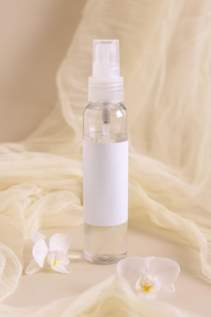 Spray refillable bottle near orchid flowers and tulle on light beige Cosmetic packaging Mockup