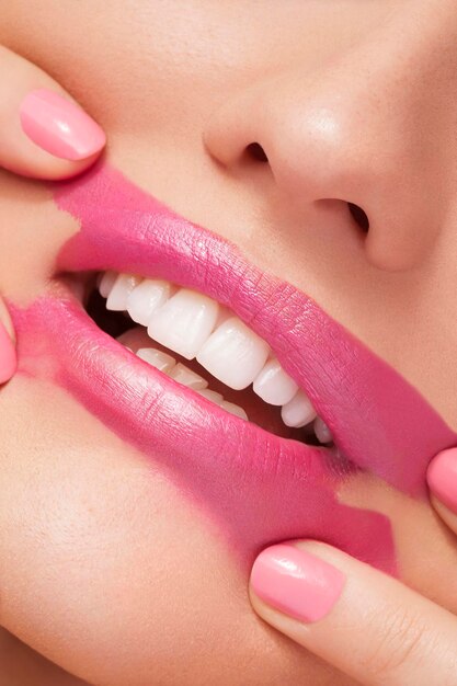 Spreading pink lipstick on face in close up photo