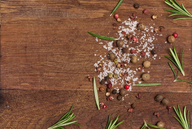 Sprigs and leaves of rosemary a mixture of peppers and salt on a wooden background top view