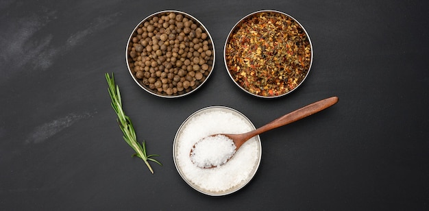 Sprigs of rosemary, salt and pepper in an iron plate on a black surface, top view, banner