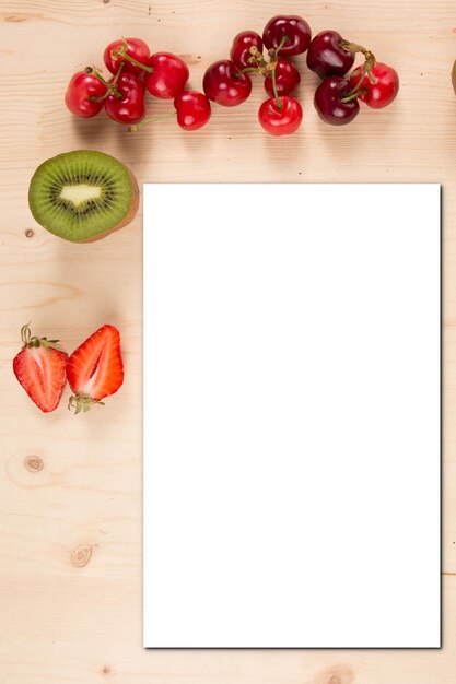 テキストの空白の白い紙と春の抽象的なイチゴチェリーキウイフルーツの背景食品は空の白いグリーティングカード紙の招待レシピをモックアップ