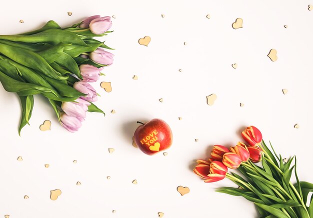 Primavera bellissimi fiori di tulipano su sfondo chiaro morbido con cuori di legno e mela rossa con scritta ti amo. festa della mamma, composizione floreale decorativa festiva della cartolina d'auguri.