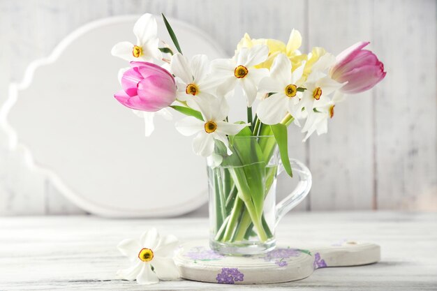 木製の背景の色にガラスのマグカップで春の花束