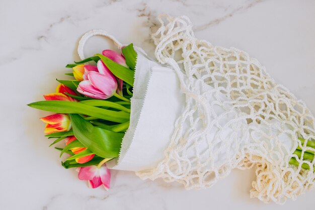 Spring bouquet of multicolored tulips in eco bag on a marble background. Copy space, flat lay background.