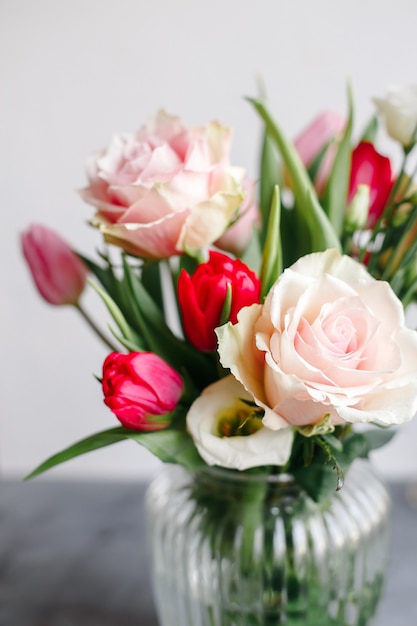 Spring bouquet in transparent glass vase. Roses, tulips and lisianthus.