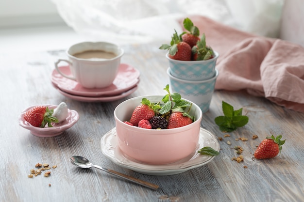 Spring Breakfast with granola and fresh strawberries and lychee and flowers on wooden background.