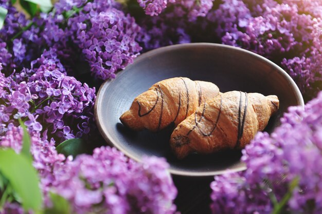 Spring cet and fresh breakfast on a wooden table.Siren croissants are on the table. A bouquet of lilac on a wooden table.