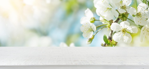 Photo spring cherry blossoms with empty wooden white table and spring apple garden on the backgrounds happy easter or passover card wide banner with copy space for product presentation showcase