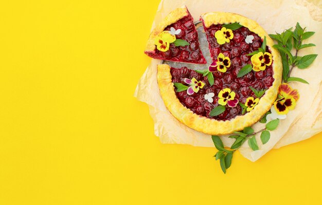 Spring cherry pie, decorated with edible flowers on a yellow. 