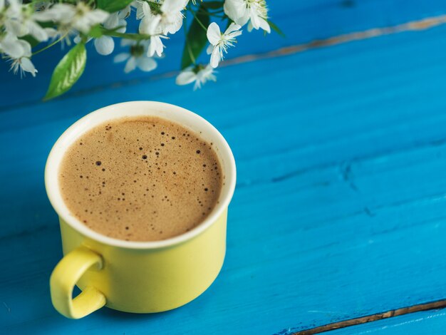 Spring coffee . yellow cup on blue background and cherry blossoms