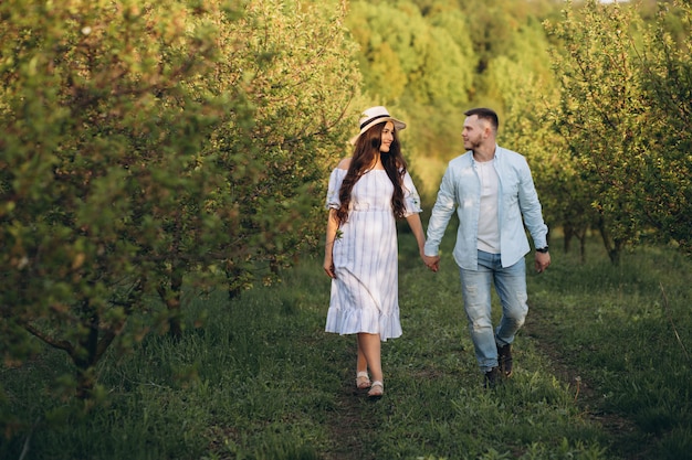 Spring coming! Beautiful young cheerful couple man and pregnant woman in wreath flowers on head hugging in spring tree garden. Beauty People Lifestyle Family concepts. Happy mom in waiting for baby!