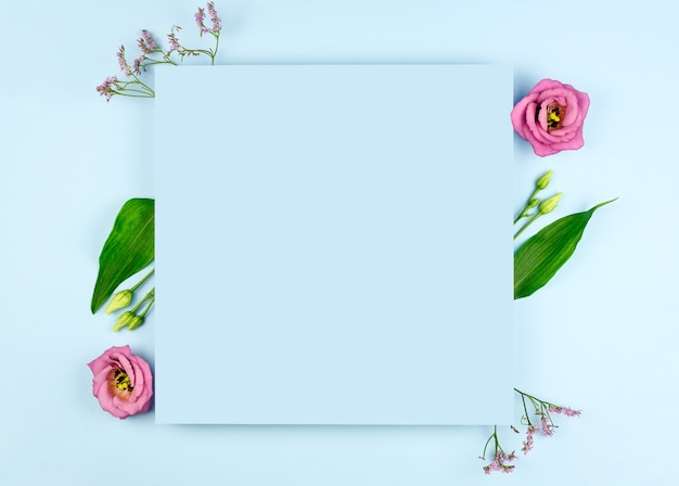 Spring composition. Pink flowers, paper blank on pastel blue background. Flat lay, top view, copy space, mock up. 