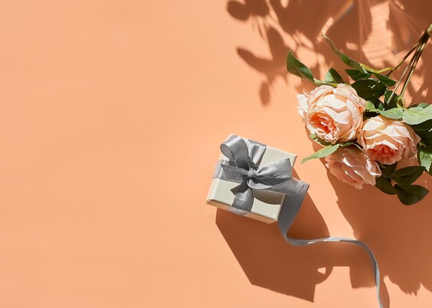 Фото Весенняя композиция с цветами и подарочной коробкой с лентой на пастельном персиковом фоне