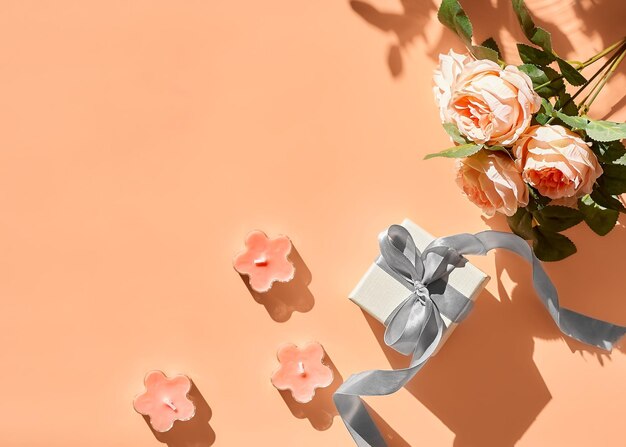 Photo spring composition with flowers and gift box with ribbon on pastel peach background