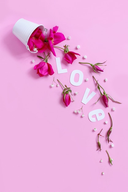 Spring composition with pink flowers and text LOVE falling from white bucket