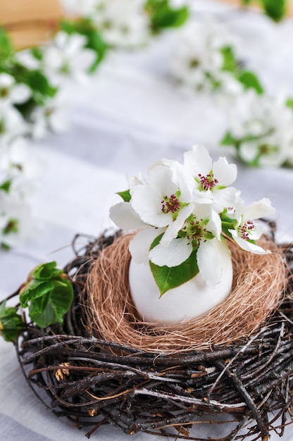 Photo spring easter composition of flowers in a white egg in a nest of branches on gray tablecloth.