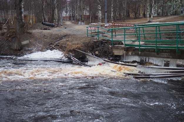 Foto inondazione primaverile acqua di corsa nel fiume acqua ferrosa scura corsa nel ruscello carelia fiume lososinka in primavera inondazioni tsunami e cambiamenti climatici ponte distrutto con tubi disastro meteorologico