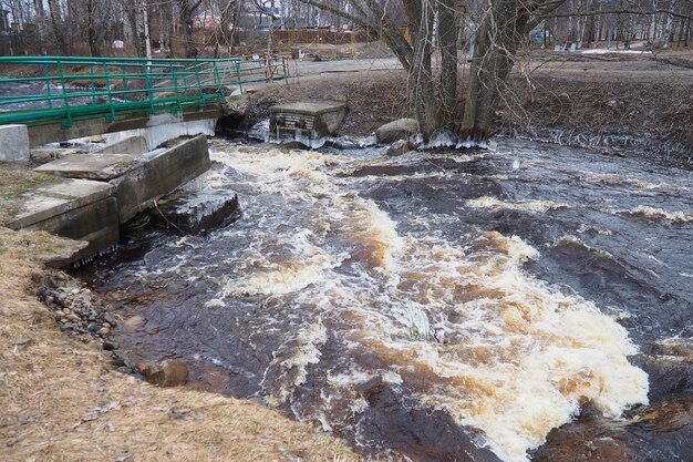 Photo spring flood rushing water in the river dark ferrous water rushes in the stream karelia lososinka river in spring floods tsunami and climate change destroyed bridge with pipes weather disaster