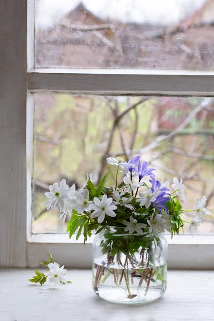 Spring flowers in glass jar on window