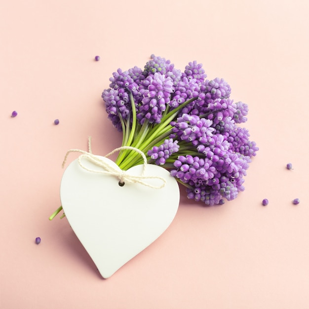 Spring flowers and a heart-shaped empty card on pink background