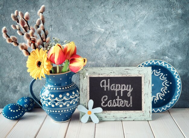 Фото Весенние цветы в синий керамический кувшин с соответствующей пластины и пасхальные яйца и доске.