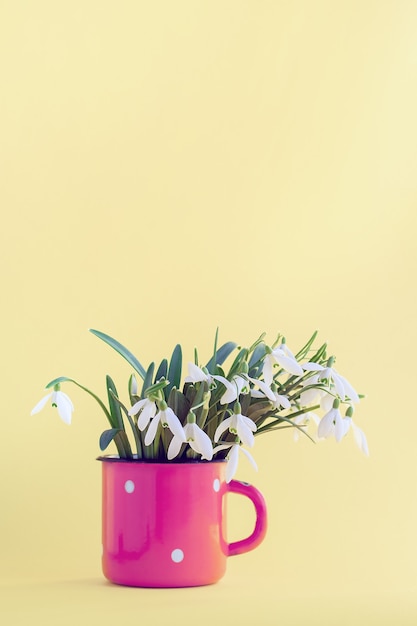 Spring flowers in a pink mug on a yellow wall.