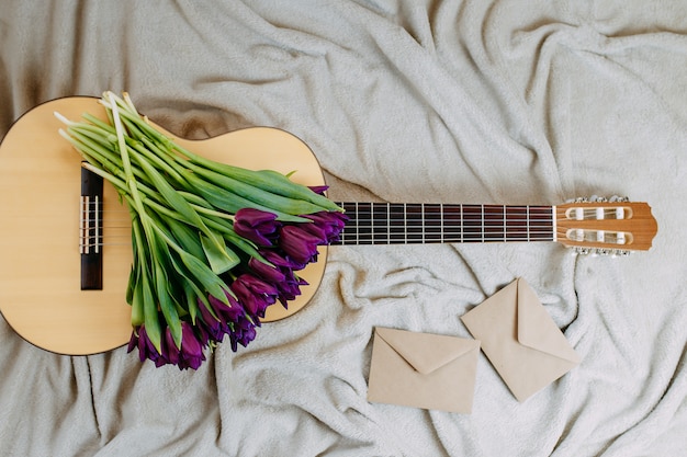 Весенние цветы, фиолетовые тюльпаны, белая гитара и цветы на сером фоне, весенний музыкальный плакат, букет фиолетовых тюльпанов на гитаре, конверты из крафт-бумаги.