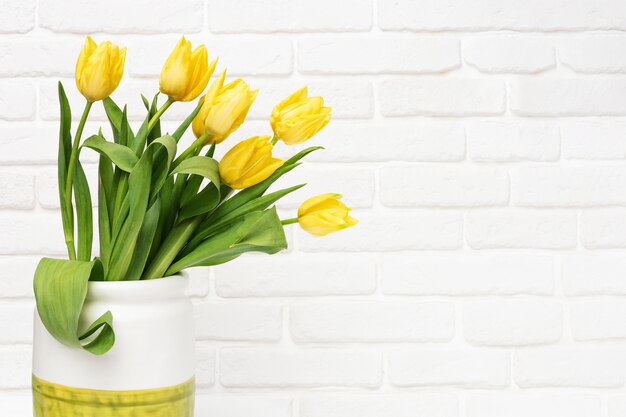 Fiori di primavera di tulipano in vaso decorativo sul muro di mattoni