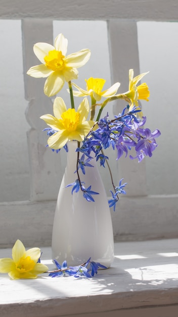 Spring flowers in vase on white wooden bench