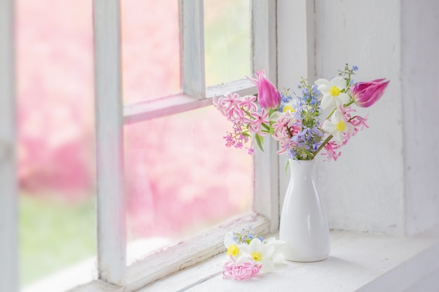 Spring flowers in white vase on old windowsill