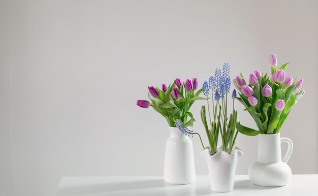 Photo spring flowers in white vases in white interior