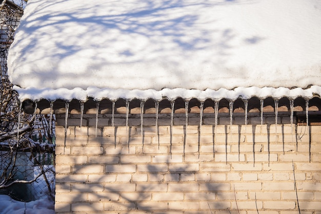 Spring ijspegels die van het dak van de oude bakstenen huizen met sneeuw bedekt dak hangen