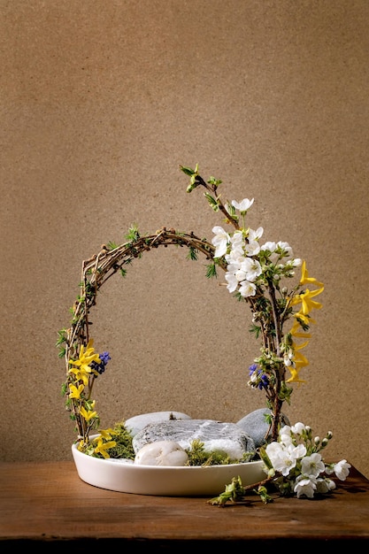 봄 이케바나 꽃 아치 구성은 봄에 피는 흰색과 노란색 꽃 가지와 갈색 나무 테이블에 서 있는 흰색 세라믹 그릇에 있는 돌 일본식 가정 장식 복사 공간