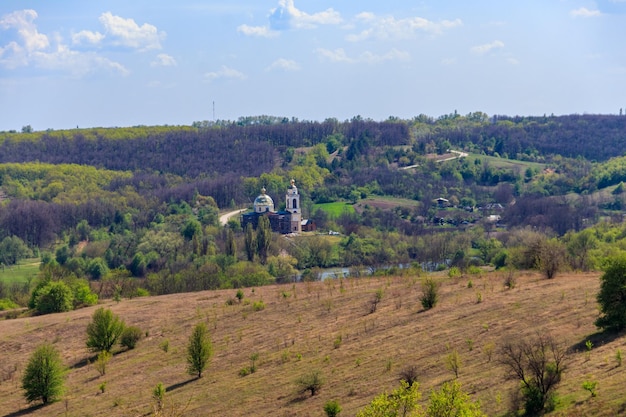Весенний пейзаж с лесными лугами, озером, небольшой деревней и православной церковью в Центральной Украине