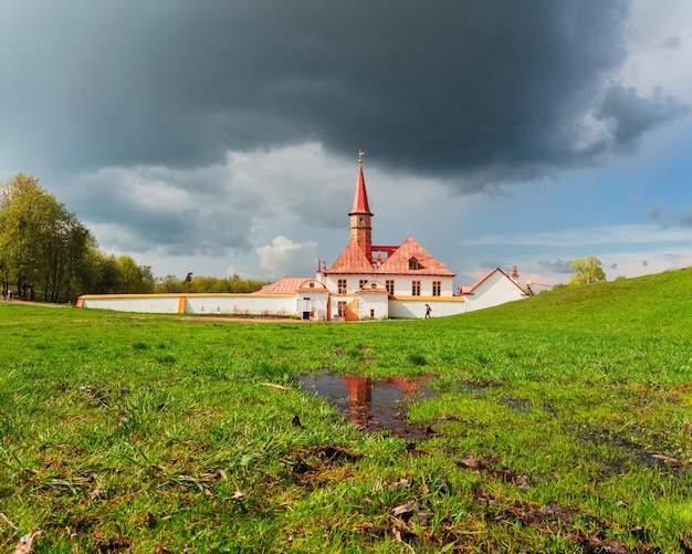 Spring landscape with wet green lawn near the white old Maltese palace Big puddle in the spring Sunny spring view of the ancient Maltese Palace in Gatchina Park Russia