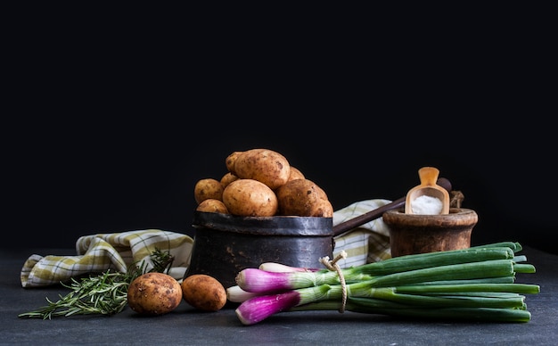 Spring onions and potatoes on dark background