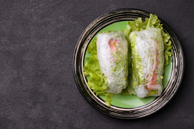 Photo spring rolls on green plate next to a gray sauce on black.