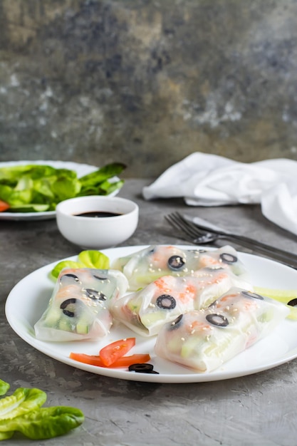 Спринг-роллы в рисовой бумаге из креветок, оливок, салата и овощей на тарелке по вертикали