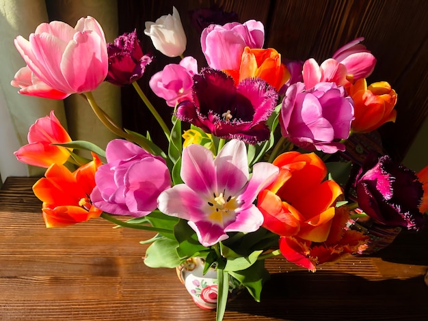 Spring romantic bouquet with garden colorful tulips in the interior on a wooden table near the window