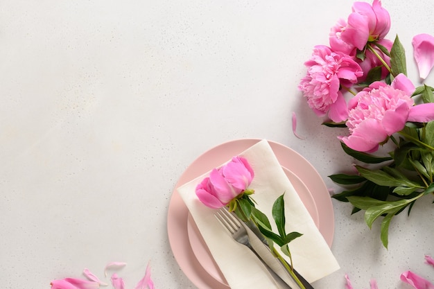 Tavola romantica primavera con fiori di peonia rosa su un tavolo bianco.