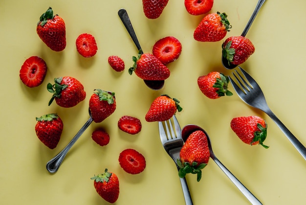 Spring season strawberry and forks on yellow background. Above view