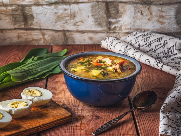 Фото Весенний суп с куриным бульоном с овощами и травами на темно-голубой тарелке