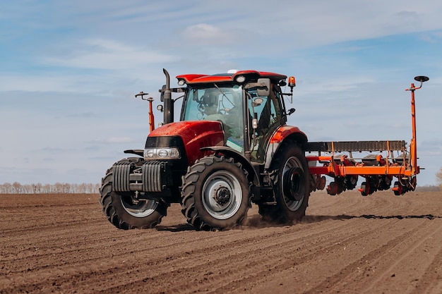 Spring sowing season farmer with a tractor sows corn seeds on
his field planting corn with trailed planter farming seeding the
concept of agriculture and agricultural machinery