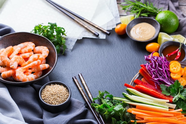 Spring or summer rolls preparation with rice paper, carrot, chili sauce, red cabbage, zucchini , pepper, shrimps and kumquats. Tasty asian food.