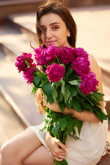 Foto stile primavera / estate. bella giovane donna bruna in un bel vestito di primavera con un mazzo di pioni. bella spring street. foto di moda primavera estate.