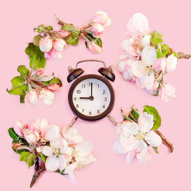 Photo spring and summer time alarm clock and flowers of apple tree on pink background